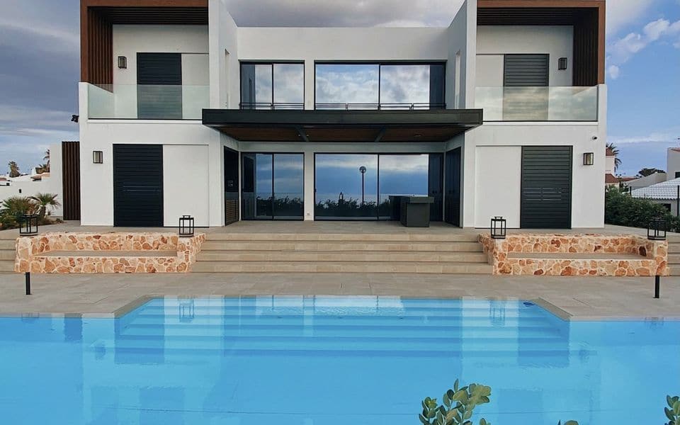Modern villa facade with glass balustrades, stone planters and a pool